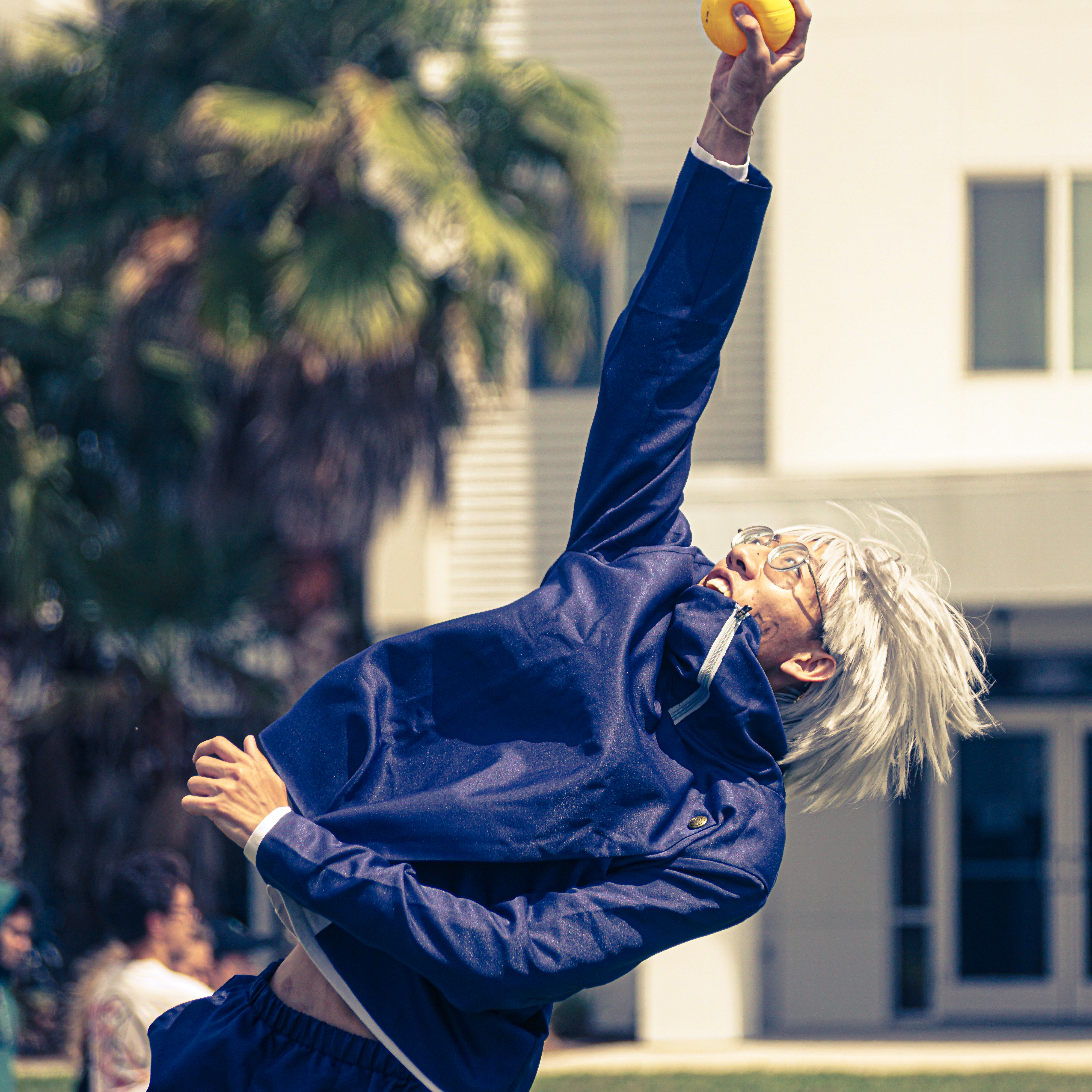 A cosplayer flings his body back to reach up to catch a ball.