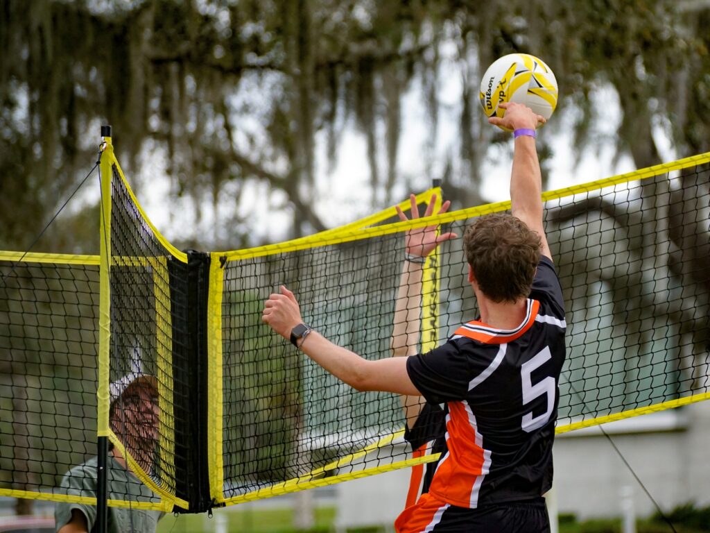 A volleyball in a black and orange uniform player reaches up to hit the ball.