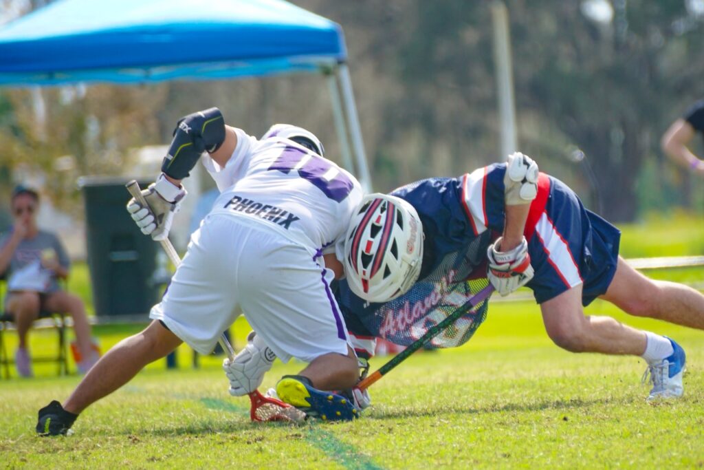 Two lacrosse players ram against each other on the grass.