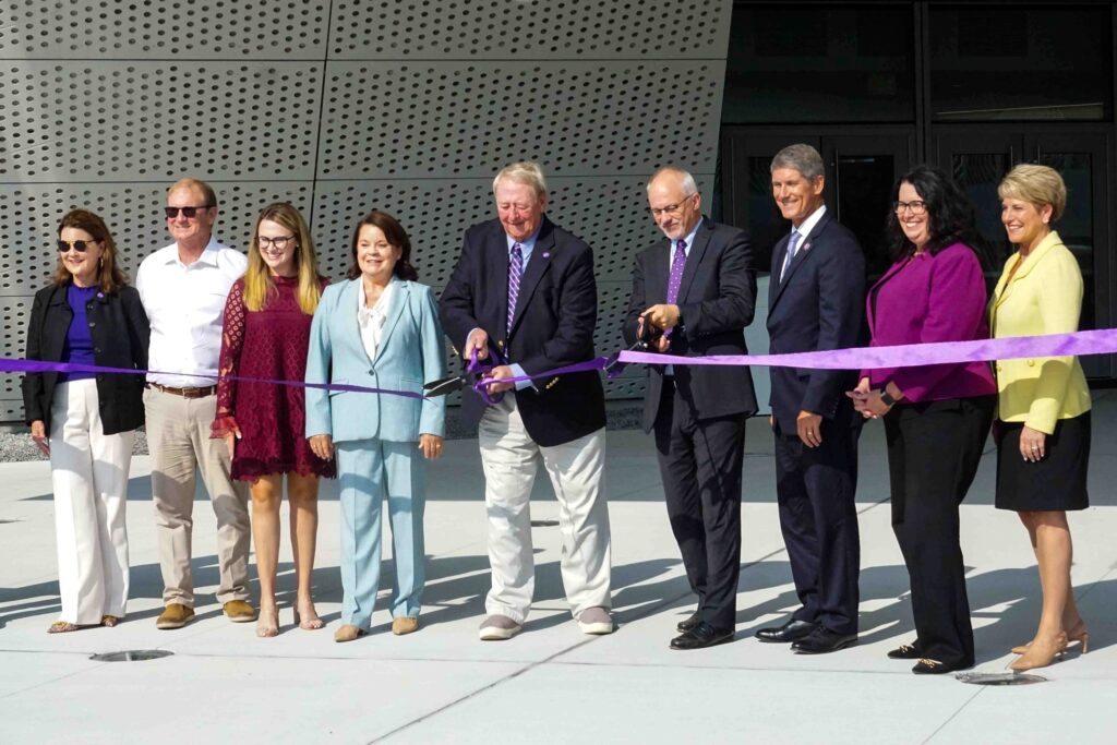 9 people in formal wear cut a purple ribbon with large scissors.